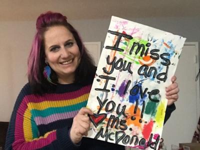 Ms. McDonald, Art Teacher holding a "I miss you" sign
